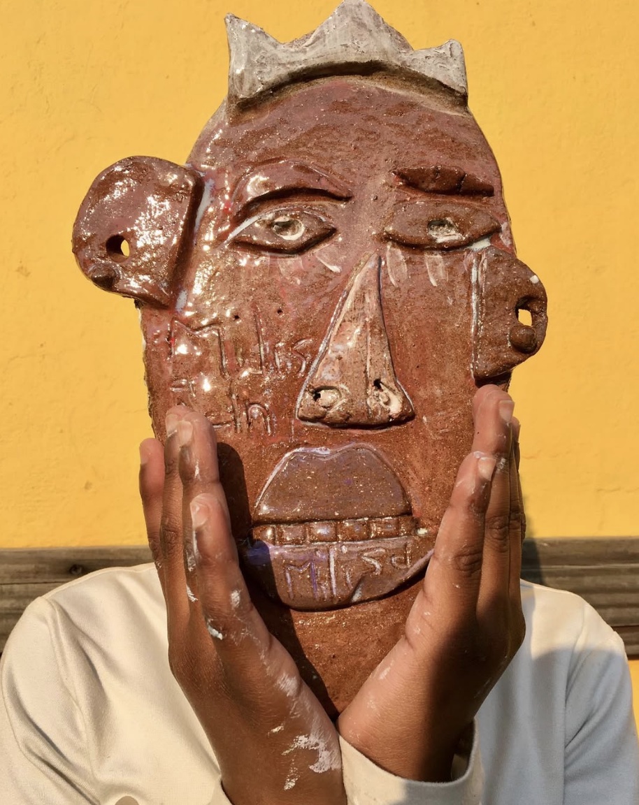 A young maker holding a clay portrait inspired by Qamatha